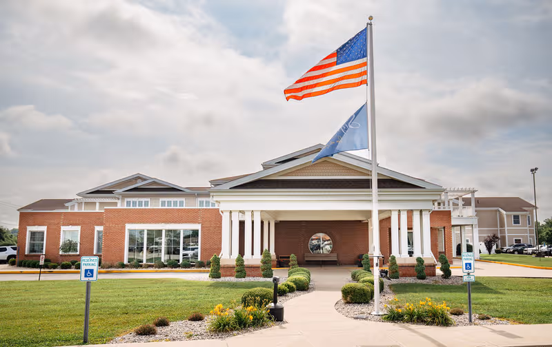 Front view of Sunrise Manor Nursing Home with flags and landscaped path.