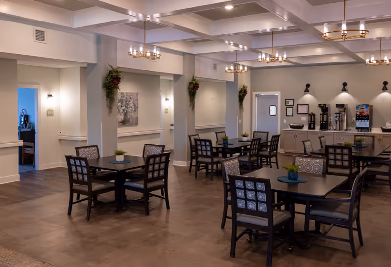 A spacious senior dining room with multiple tables, chairs, and a beverage station.