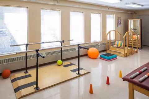 Interior therapy room with parallel bars, mats, balls, and cones at Bradford Square.