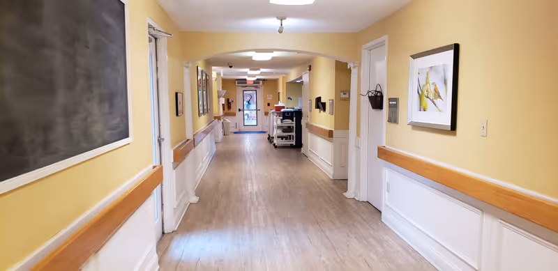 Bright hallway in a senior care facility with yellow walls and wooden rails.