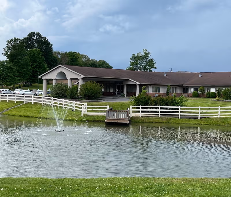 A single-story facility with a brown roof sits beside a pond with a fountain.