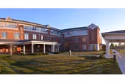 Exterior view of a large three-story brick building with multiple windows and a covered entrance, surrounded by a grassy lawn under a clear blue sky.
