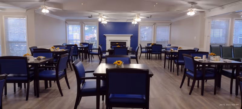 Bright dining room with multiple tables, blue chairs, and a fireplace backdrop.