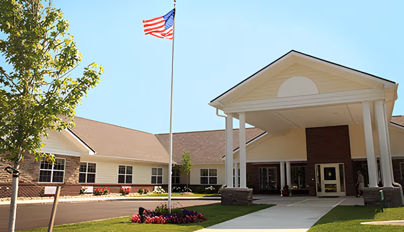 Front entrance of The Willows at Citation with a covered porte-cochère, American flag, and landscaped lawn.