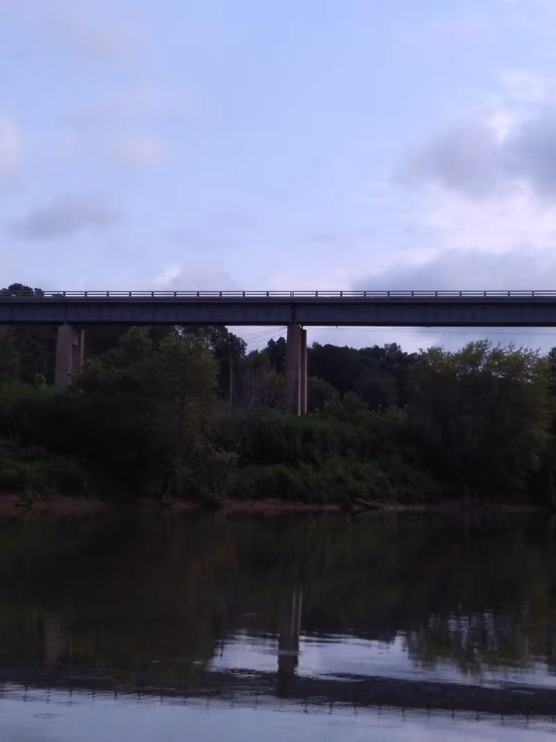 A bridge over a river with trees and a cloudy sky.