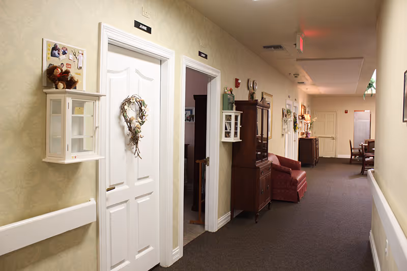 Long hallway inside a senior living facility with doors, furniture, and soft decor.