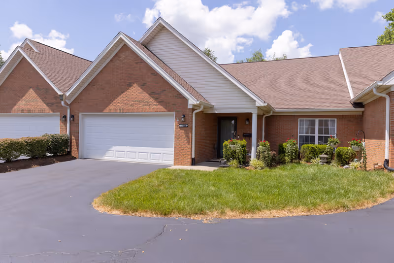 Front view of a brick senior living facility with a two-car garage and landscaping.