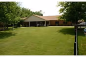 Single-story brick nursing facility with a covered front porch facing a large grassy lawn and trees.