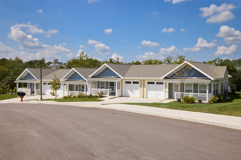 Single-story row of attached residential units with garages and porches on a sunny day.