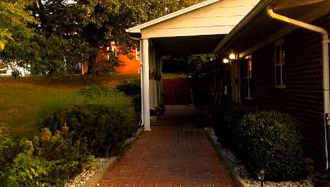 Brick walkway to a covered entrance of a senior living facility, with shrubs along sides.