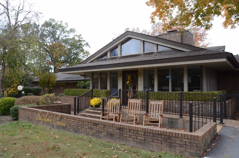 Front exterior of the Southern Grace Assisted Living building with a brick facade, porch area with rocking chairs, and a low brick wall displaying the facility name.