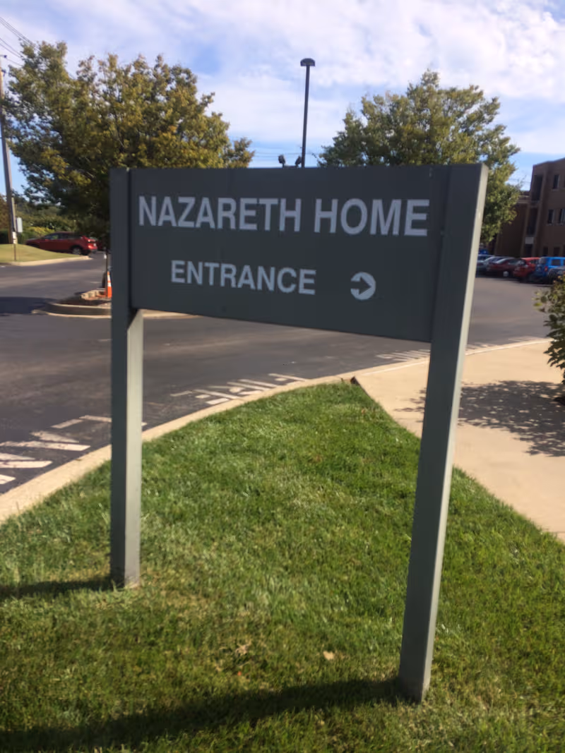 Nazareth Home Entrance sign on a grassy median by a parking lot