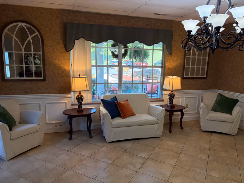 Cozy living room lounge with three armchairs, side tables, lamps, and a large window.