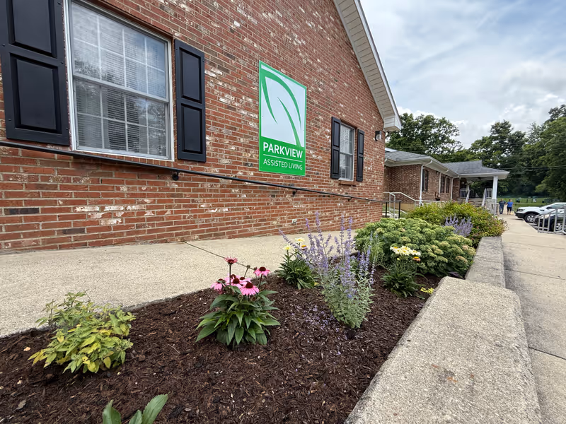 Brick exterior of Parkview Assisted Living with a landscaped flower bed along a sidewalk