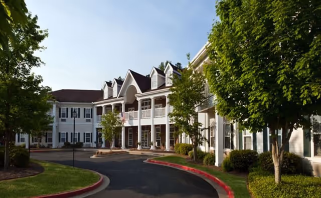 Exterior view of a Wesley Village Senior Living building with trees and a curved driveway.